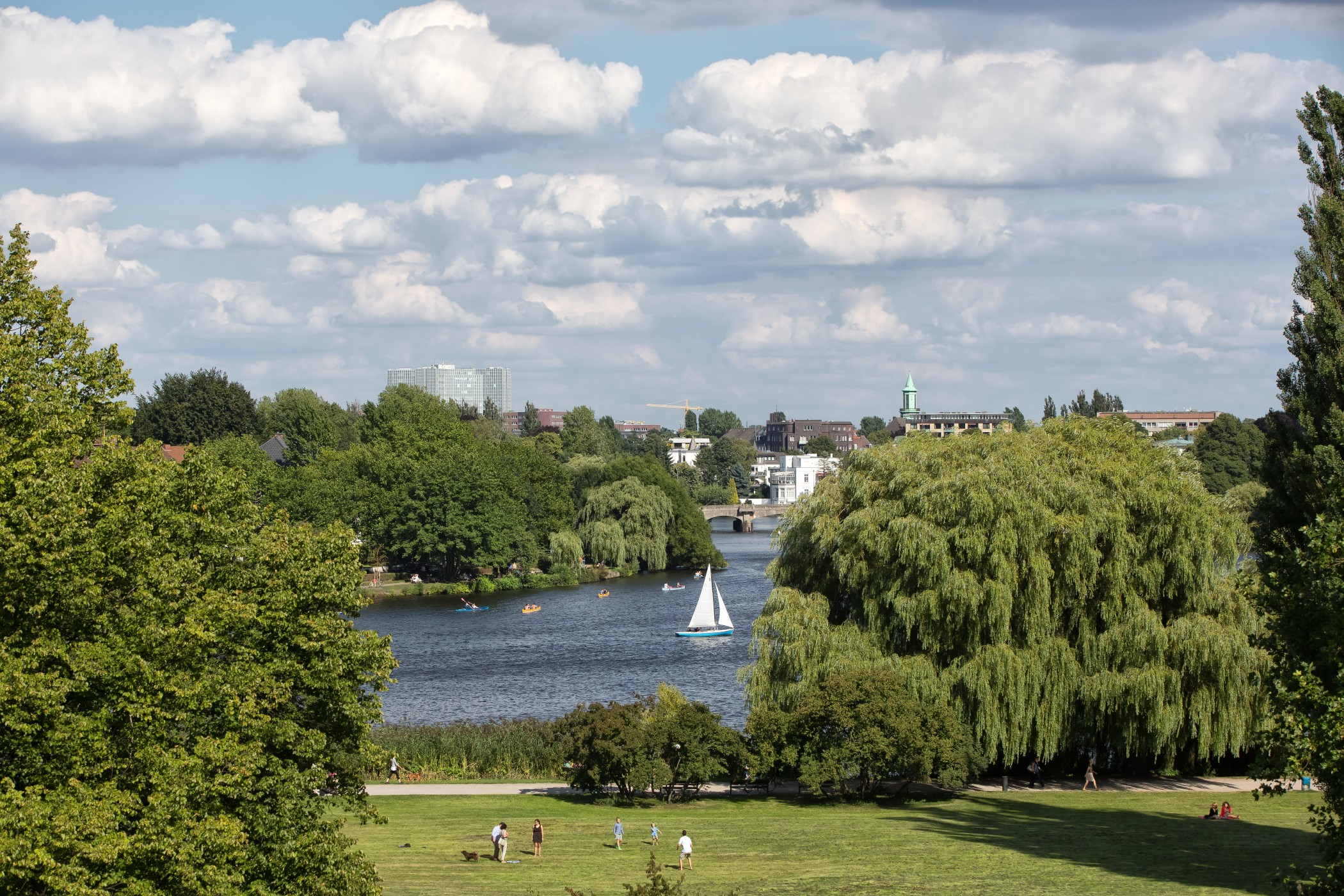 View across the Alster meadows to the Alster with a sailing boat